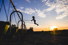 Full Length Of Girl Swinging On Swing At Playground During Sunset