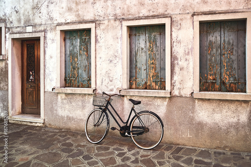 Fototapeta na szkło Old rusty bicycle against the old wall on the street. Italy, Venice, Burano island