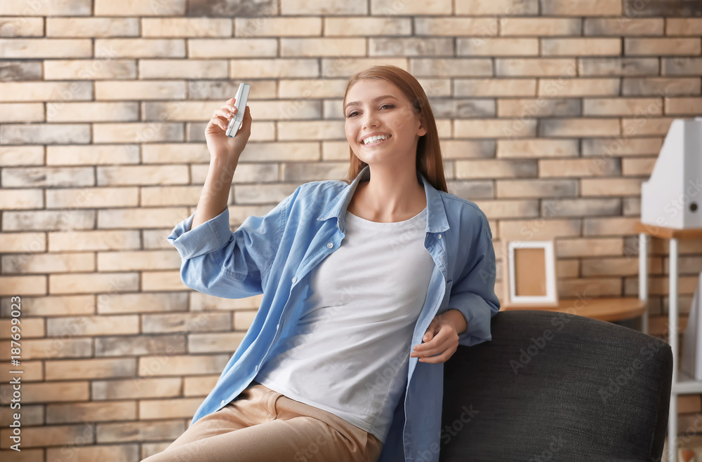 Young woman switching on air conditioner at home