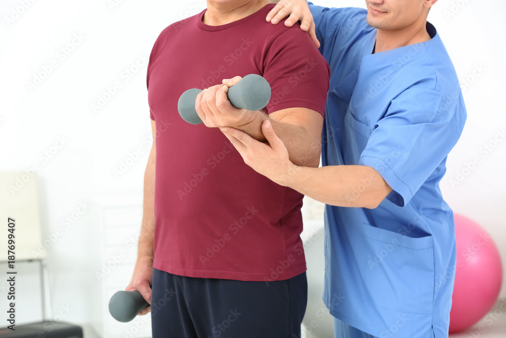 Senior man doing exercise under supervision of physiotherapist, closeup