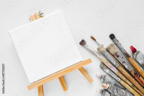 Canvas On Easel Paint Tubes And Bundle Of Brushes For Painting On