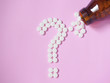 Question mark made by white pills spilling out of brown glass bottle on pink background. Creative medicine for health/medical problem, drug interaction, medication error and pharmaceutical concept.