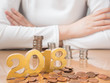 2018 new year financial resolutions and money planning concept. Female in white shirt w/ crossed arm saving money for investment, travel or home w/ gold number 2018 and pile of coins on wood table.