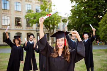 Wall Mural - We did it! Happy grad girl is smiling, group of her friends class mates are behind. She is in a black mortar board, with red tassel, in gown, with nice brown curly hair, diploma in hand