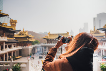 Wall Mural - Tourist woman taking photo picture at temple in shanghai, china. Young asian woman in jacket clothes using camera take a picture of Jing'an temple in shanghai.