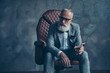 © deagreez - Minded, ponder, unhappy rich man in glasses, hold glass with cognac, in tuxedo with red bowtie and pocket square, sit in leather chair over gray background, looking to the side, shares, stock, money