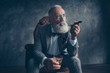 © deagreez - Minded, ponder rich man in glasses, smoke cigarette, fume, hold glass with brandy, in tux with red bowtie, sit in leather armchair over gray background, looking to the side, shares, stock, money