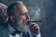 © deagreez - Side view close up of brutal harsh professional investor, shareholder smoking cigar over gray background