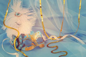 Image of delicate elegant venetian mask over blue silk and tulle fabric background.