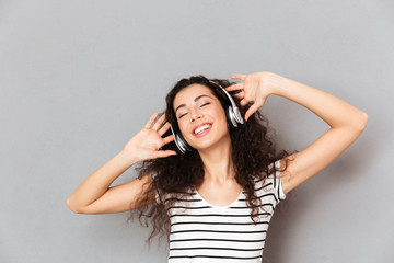 Sticker - Picture of pleased young woman in striped t-shirt enjoying favourite songs listening melodies via headphones with closed eyes over grey background