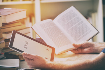 Man holding a modern ebook reader and book in library