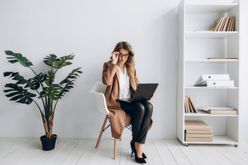 Amazing business woman sits on a chair with a laptop in her office with a bright interior