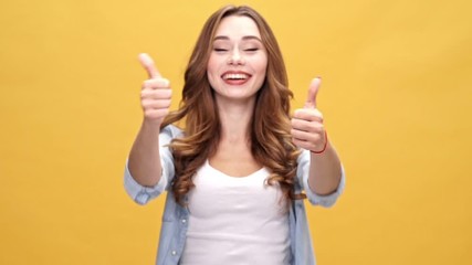 Poster - Happy brunette woman in denim shirt showing thumbs up and looking at the camera over yellow background