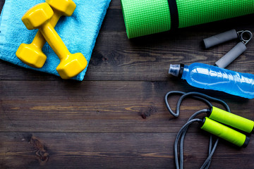 fitness equipment. jump rope, dumbbells, expander, mat, water on dark wooden background top view cop