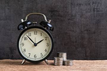 Alarm clock with money stack of coins on wooden table and black background as long term or time for retirement invest concept with copy space