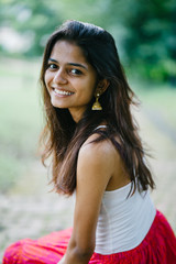 Wall Mural - Portrait of young Indian woman smiling and sitting in a park (Fort Canning Park in Singapore) in the day. She is attractive and is dressed in a summer outfit.