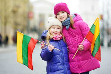 Two adorable little sisters celebrating Lithuanian Independence Day holding tricolor Lithuanian flags