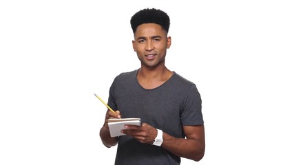 Poster - Concentrated smiling african man in t-shirt interviews and writing something in notebook over white background