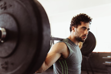 Healthy young guy at gym exercising with barbell