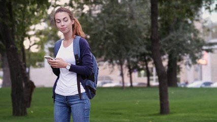 Poster - Cheerful brunette woman with backpack writing message on smartphone in park