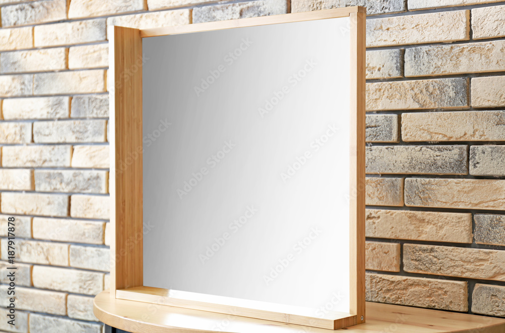 Modern mirror on stand near brick wall