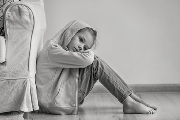 Wall Mural - Sad little girl sitting on floor indoors, black and white effect