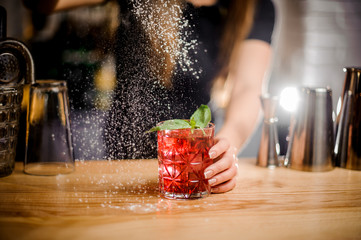 barmaid finishes cocktail preparation by adding a bitter of powdered sugar