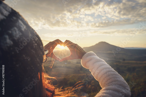 Fotografía Young woman traveler making heart shape symbol at sunrise
