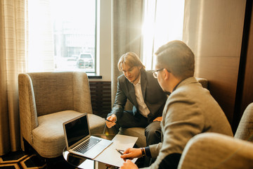 Two male employees consulting with laptop in cafe or office
