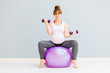 © Iryna - Happy smiling pregnant woman sitting on fitness bal and working with dumbbells. Full body. Sport, maternity and liesure concept.