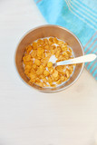 Fototapeta Dziecięca - Cornflakes in a metal bowl with milk on a painted white wooden background. Composition with a dish towel and spoon.