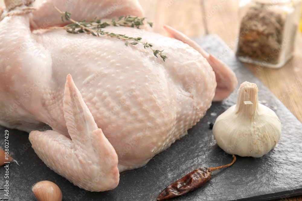 Slate plate with fresh whole chicken, thyme and spices on table