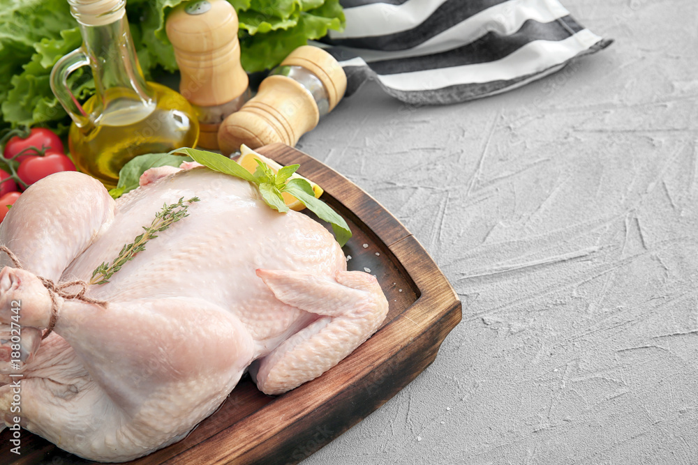 Wooden board with whole chicken and herbs on table