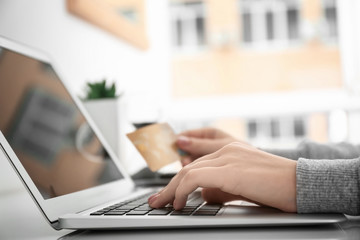 Wall Mural - Woman using laptop while holding credit card at table. Internet shopping concept