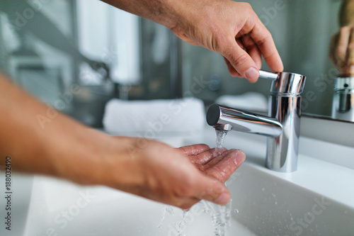 Fotomural Man washing hands in bathroom sink at home checking temperature touching running water with hand