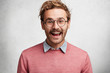 © WHstudio Leushin N - Content satisfied glad male dressed in pink sweater with shirt and spectacles has happy smile on face, being in good mood after successfully prepared project, poses against white concrete wall