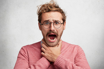 Wall Mural - Angry irritated male makes suicide gesture, keeps hands on neck, feels himself guilty, isolated over white background. Stressful concerned young man chocked by cough, stifles. Depression concept