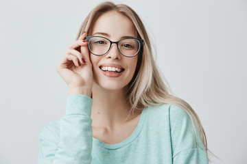 Wall Mural - Cheerful female student in stylish eyewear rejoices successfully passed exams, glad to have meeting with groupmates. Delighted beautiful pleased woman has attractive look, poses indoors.