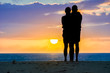 Silhouette eines Paares am Strand schaut sich gemeinsam den Sonnenaufgang über dem Meer im Urlaub an