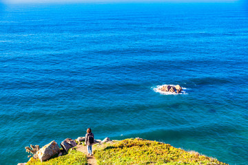 young woman on the background of the Atlantic Ocean, at Cape Cabo da Roca, Portualia. A huge ocean and a little human