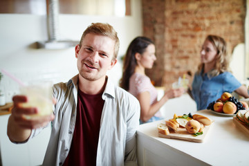 Happy guy cheering up with homemade drink with two girls talking on background