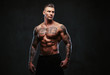© Fxquadro - A muscular tattooed man on a dark background.
