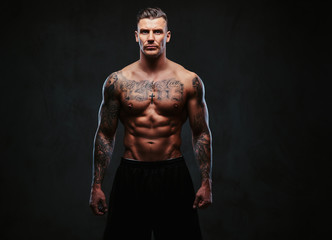 Wall Mural - A muscular tattooed man on a dark background.