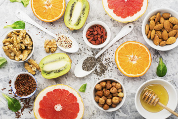 Wall Mural - Ingredients of healthy dietary food breakfast pink grapefruit, orange, chia seeds, quinoa, green herbs, kiwi, wild rice, almonds, walnuts, hazelnuts on a light marble background. The concept of