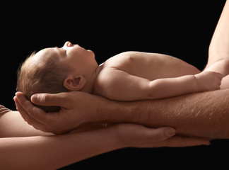 Wall Mural - Hands of parents holding cute little baby on dark background