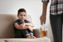 Sad Little Boy And Blurred Woman With Bottle Of Alcohol Indoors