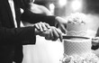 © maxbelchenko - A bride and a groom is cutting their wedding cake. beautiful cake. nicel light. wedding concept. black and white photo
