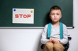 Little boy being bullied at school near chalkboard with sign STOP indoors