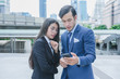 © oyoo - Profession businessman and businesswoman using smartphone for work outside office in cityscape background