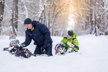 father with his son and daughter, and with two dogs the husky playing in the snow in the park in the winter.